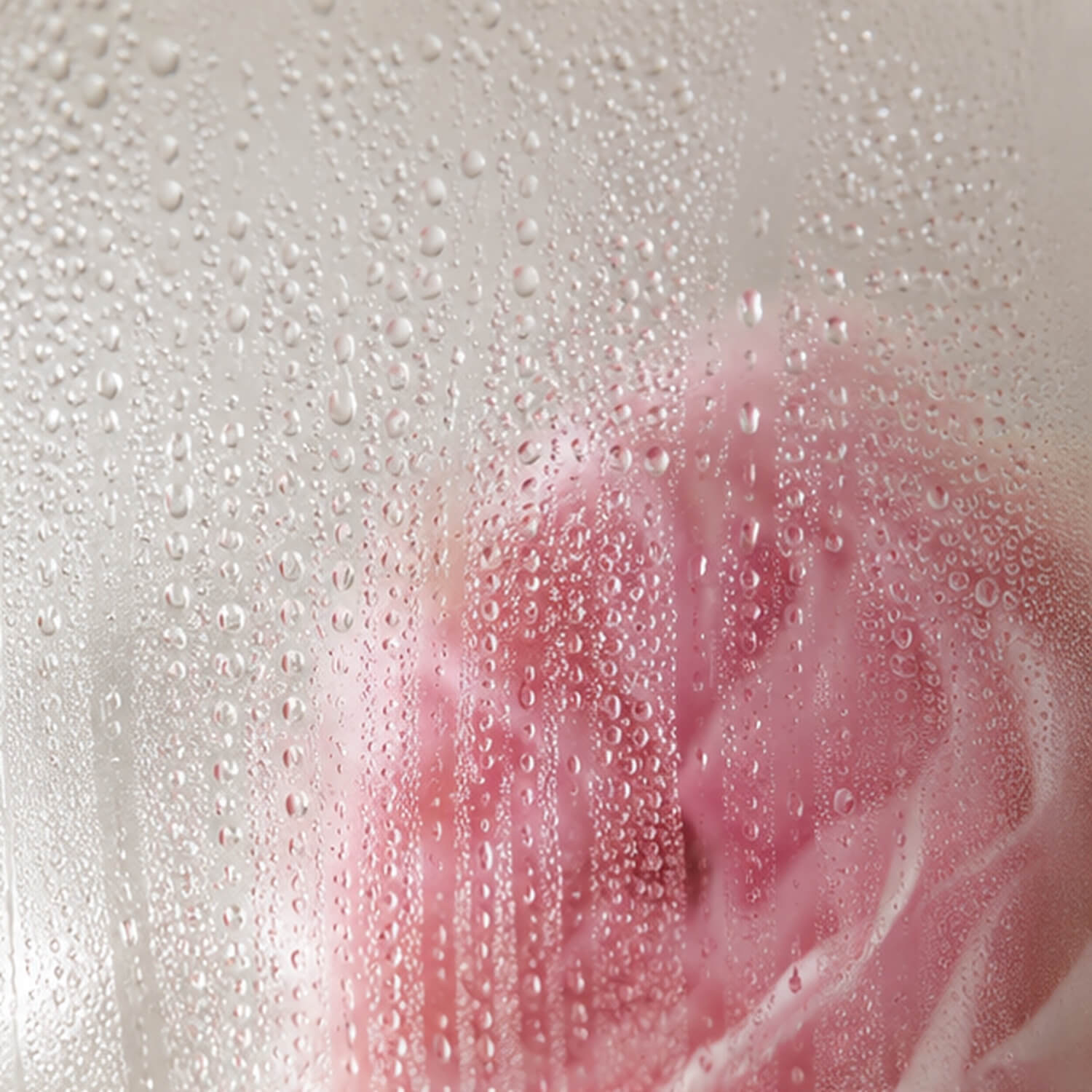 Feiner Rosenwasser-Sprühnebel und klare Wassertröpfchen auf Glas mit zartem Rosenakzent