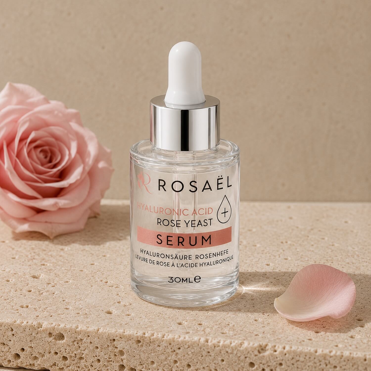 Rosaël Gesichtsserum mit Pipette auf hellem Travertinstein neben zarter Rose
